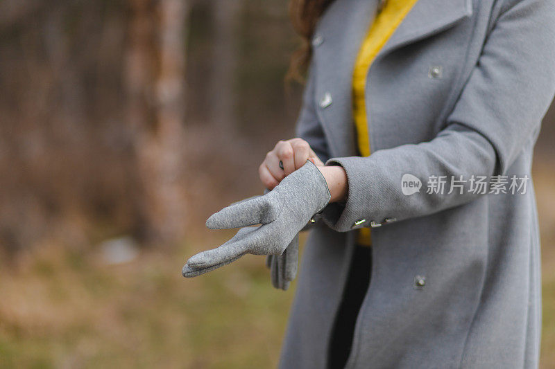 一个年轻漂亮的女孩穿着灰色的外套，在森林外面戴上手套的特写镜头