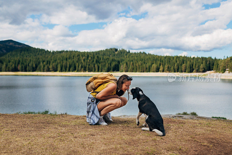 这只狗走近一位站在湖边的美丽的千禧一代女性，并亲吻她。
