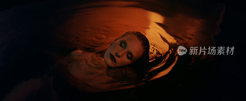 水下冥想。迷人的女人从深色、金色的水中浮现