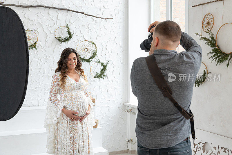 专业摄影师在摄影棚为怀孕的模特拍照。