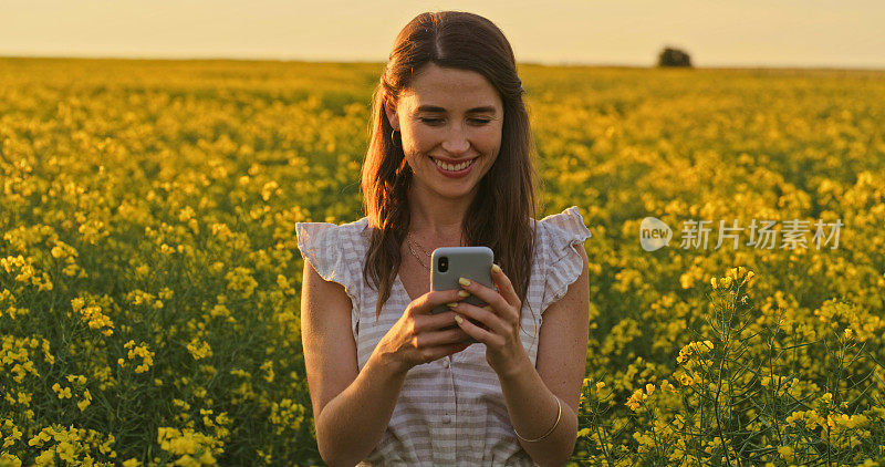 一名年轻女子在花丛中使用智能手机的照片