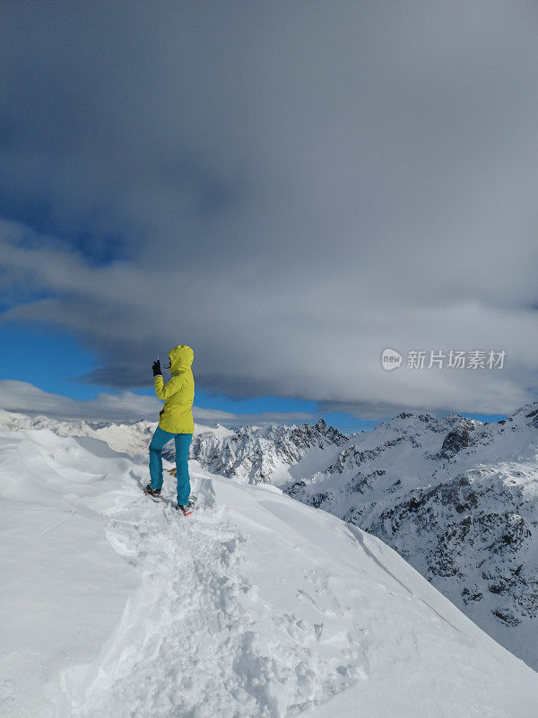 年轻女子在冬天到达山顶，她用手机捕捉了那一刻