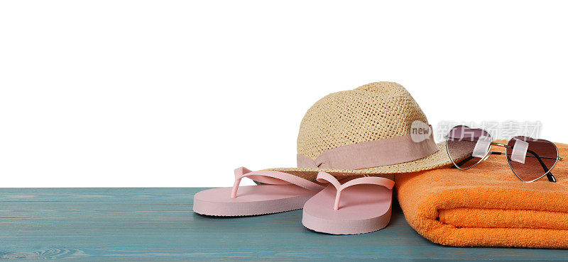 沙滩浴巾，人字拖，草帽和心形太阳镜淡蓝色木制表面上的白色背景。空间的文本