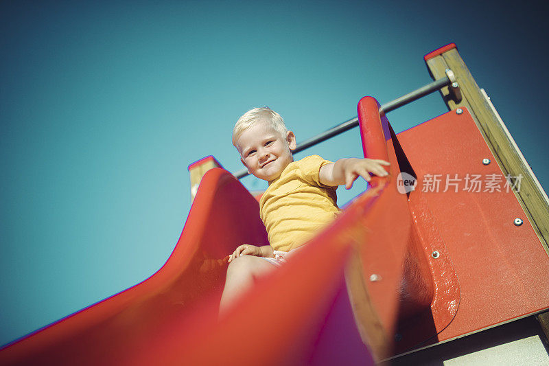 阳光明媚的日子里，小男孩在操场上玩滑梯