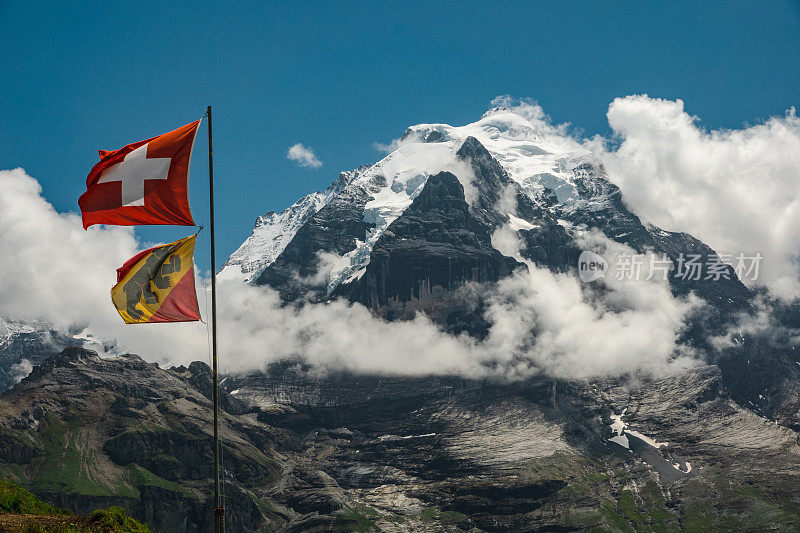瑞士伯尔尼亚斯高山的荣格弗劳山峰顶。山顶部分在云层中。前景是伯尔尼州和瑞士的国旗。