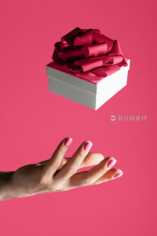 2023年度色彩，女性手扔或接白色礼品盒与蝴蝶结，万岁洋红色背景