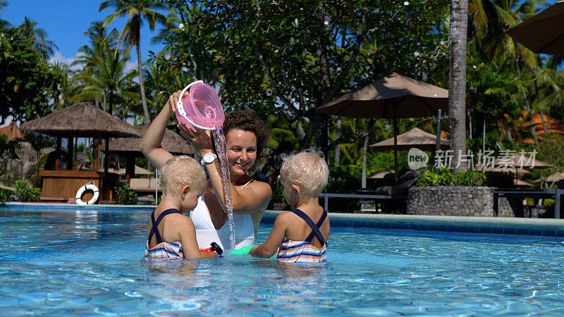 妈妈和孩子们一起在泳池里玩游泳玩具。妈妈把一个水桶举过头顶，模仿瀑布把水倒出来。让孩子们在假期忙起来的小贴士。
