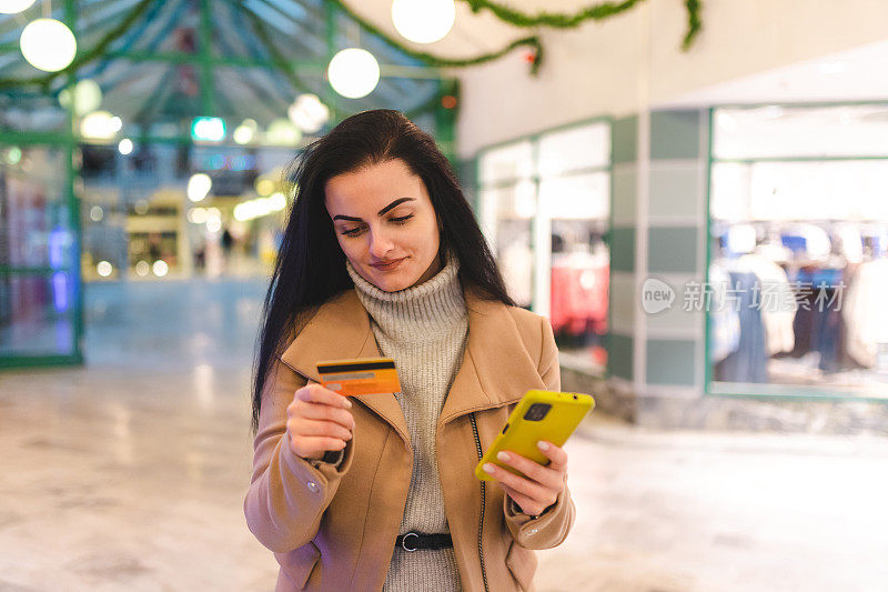 美丽的年轻女子拿着信用卡和手机在购物中心