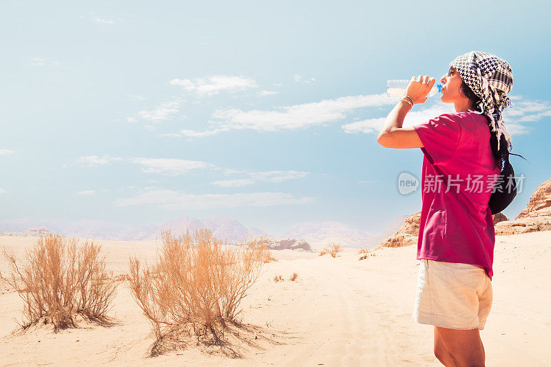 在酷热的瓦迪拉姆沙漠户外徒步旅行途中，一名口渴的白种人女子在极端高温下喝冰冷的淡水