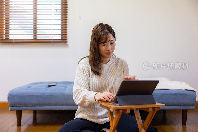 女人坐在地板上，在家里使用平板电脑