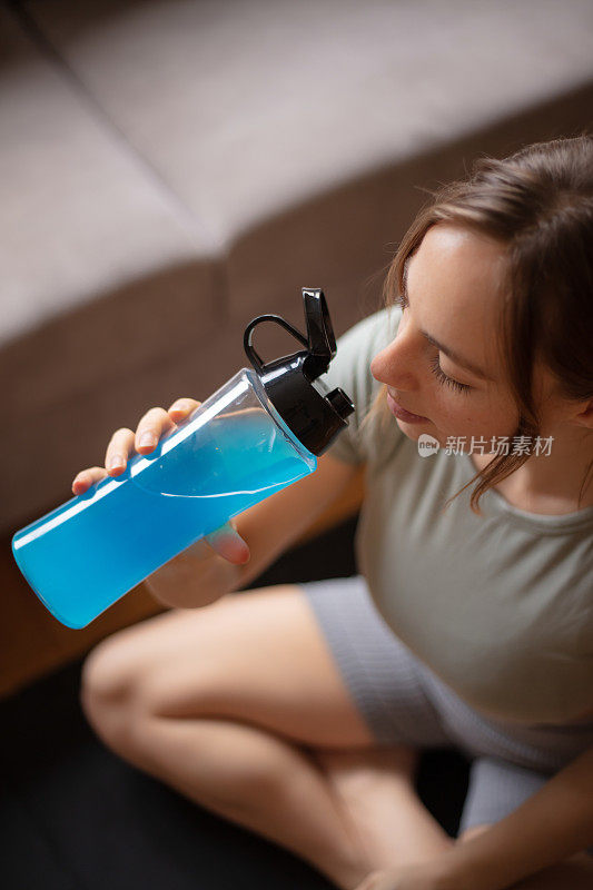 年轻女子在家里的客厅锻炼期间补水。