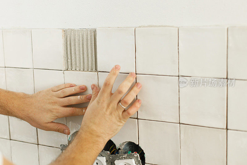 工人在插座墙上安装时尚的白色瓷砖。用手把现代方形瓷砖贴在粘合剂上。装修、家装