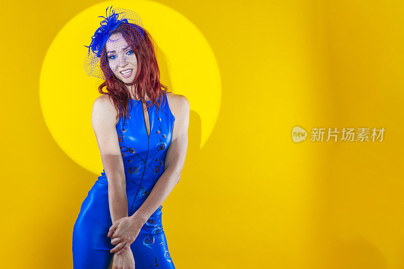 迷人的女人在蓝色艺术舞蹈服摆姿势，在披肩帽与合十的双手与圆形灯在黄色