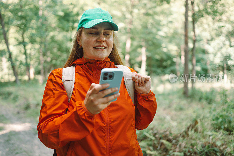 有吸引力的健康女孩游客与一个背包使用手机，而在森林里散步，做徒步旅行。远足时使用电子设备。