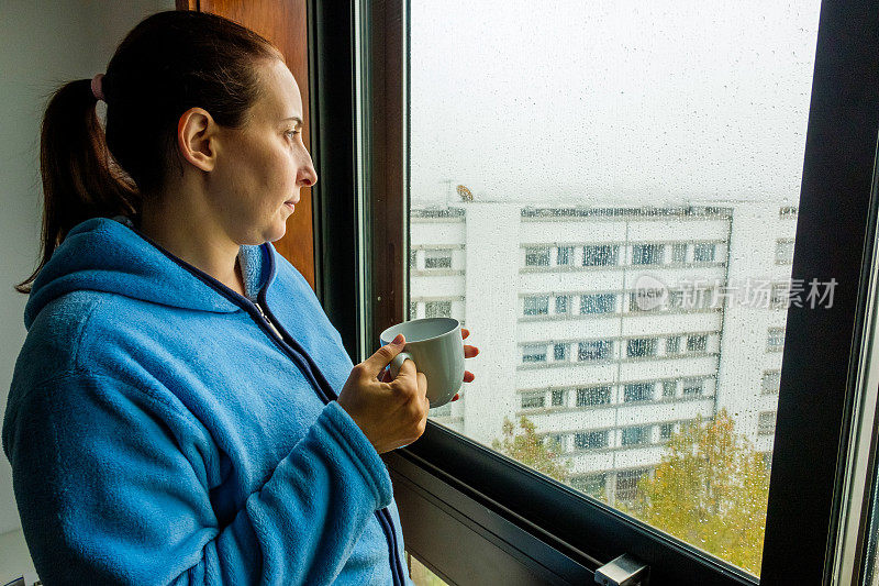下雨天，一个女人手里拿着茶望着窗外