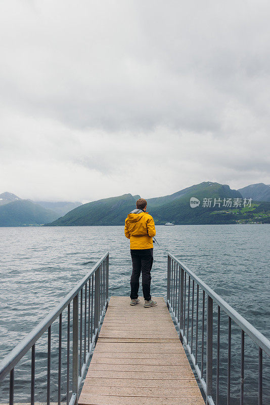 身穿黄夹克的男子在挪威峡湾边钓鱼