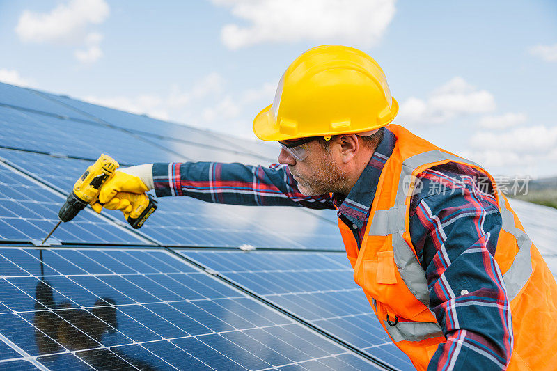 太阳能电池板安装:技术人员在工厂屋顶上与钻机一起工作