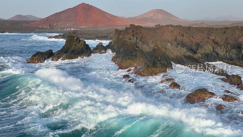 4K航拍慢镜头，湛蓝的海洋和巨大的海浪撞击岩石悬崖，溅起浪花和白色泡沫。兰萨罗特岛。西班牙加那利群岛