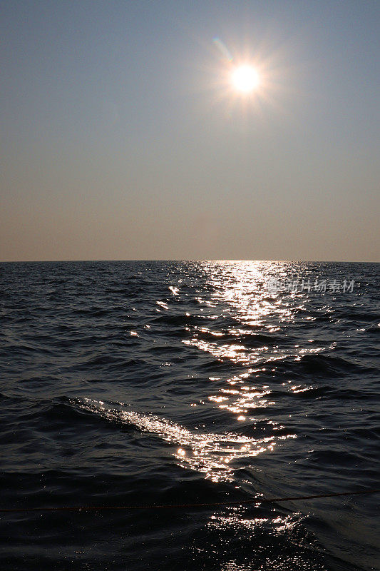 太阳在蓝色和橙色的天空中落在海上地平线上的图像，太阳在水中的反射，海面上的波浪，波涛汹涌的水面，复制空间