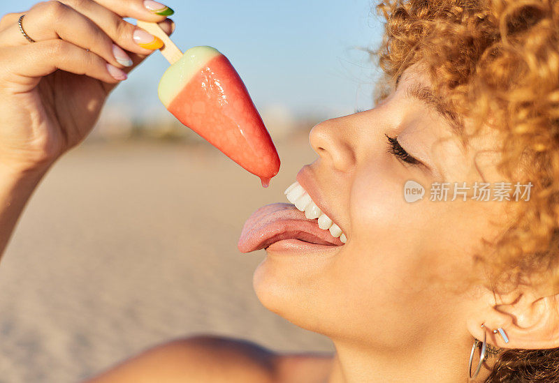 在炎热的夏日，一个微笑的年轻女子在海滩上舔着西瓜冰淇淋