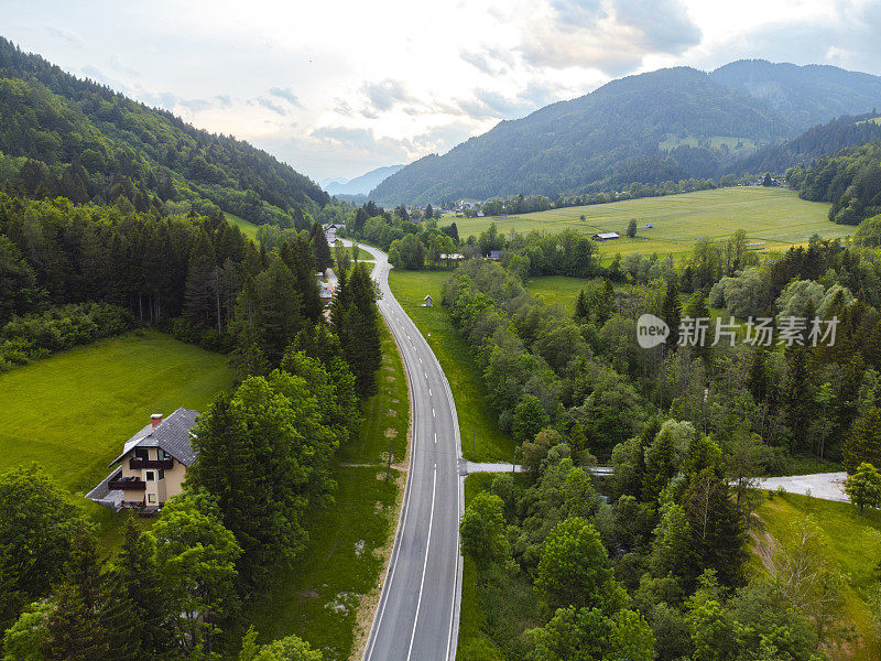 鸟瞰图，一条蜿蜒的道路穿过郁郁葱葱的绿色山谷，背景是群山。