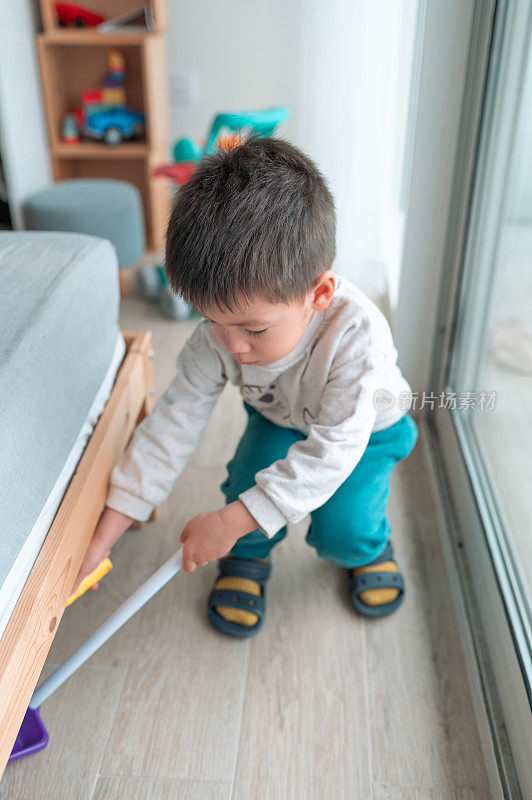 两岁半的小男孩高兴地在家里的床下扫地玩家务活动