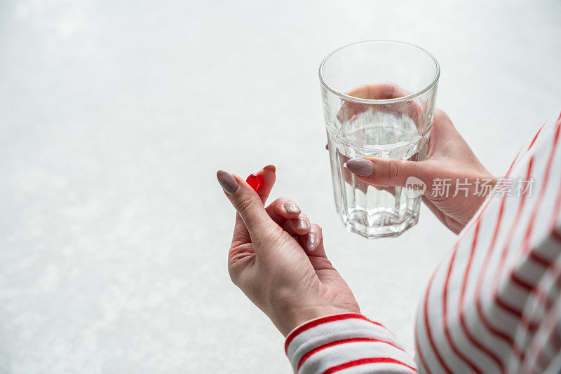 在家吃药。一个正在服药的女人。一个女人手里的一杯水和红色药丸的特写。