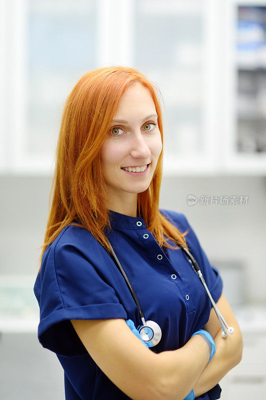 美丽的红发女医生的垂直肖像在办公室预约病人在一个现代诊所。熟练的女兽医在兽医院工作。