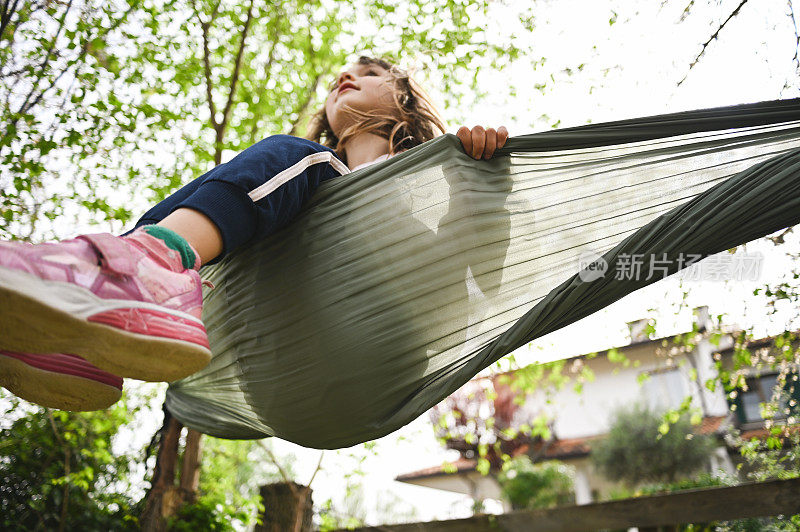 小女孩在花园里吊床上荡秋千的低角度照片。