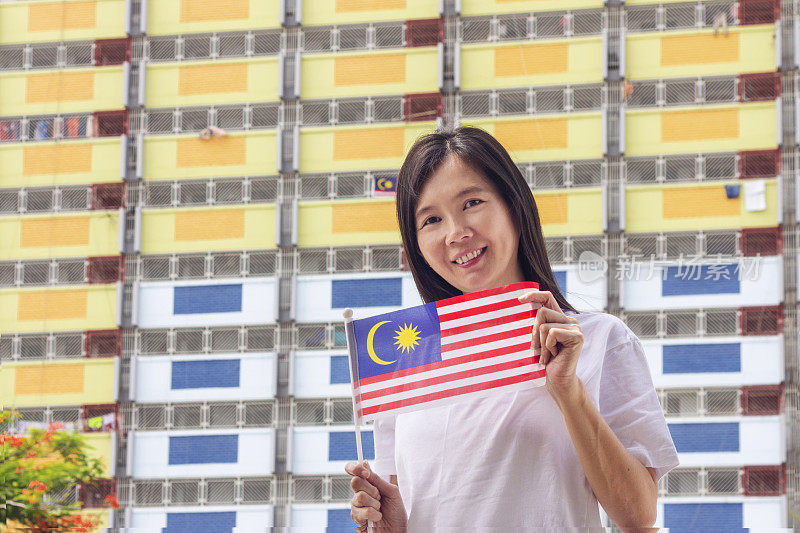 以住宅楼为背景，手持马来西亚国旗的女子