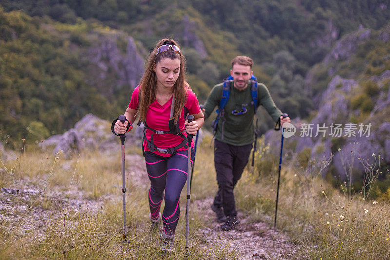 年轻的男女夫妇带着专业的装备和登山杆在美丽的大自然中徒步旅行