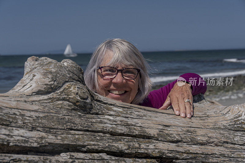 快乐的老女人在海滩上的浮木上偷看
