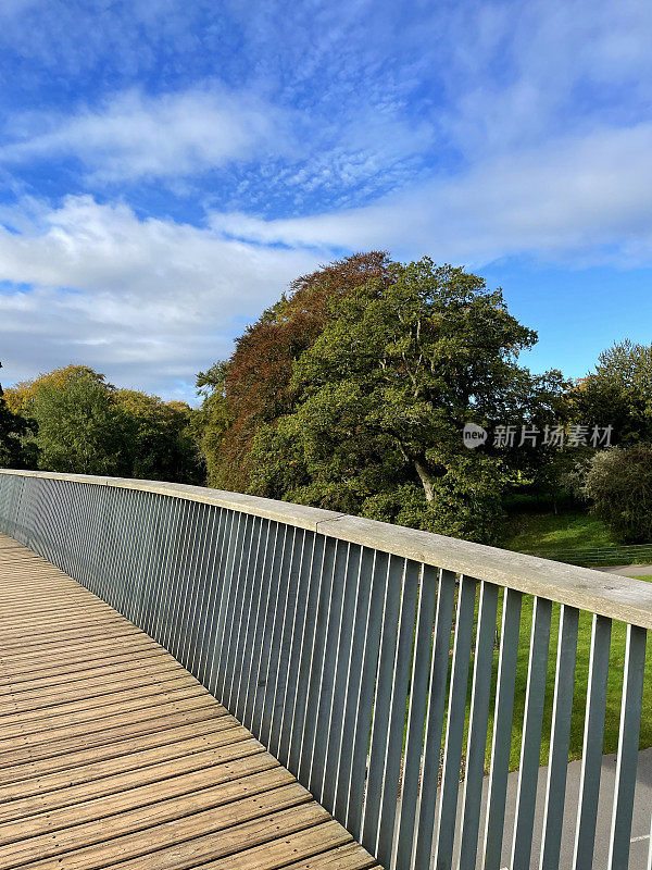 秋日阳光下的人行天桥近景，木质桥面和栏杆，木顶栏杆和金属栏杆，晴朗的蓝天下飘着松软的云朵