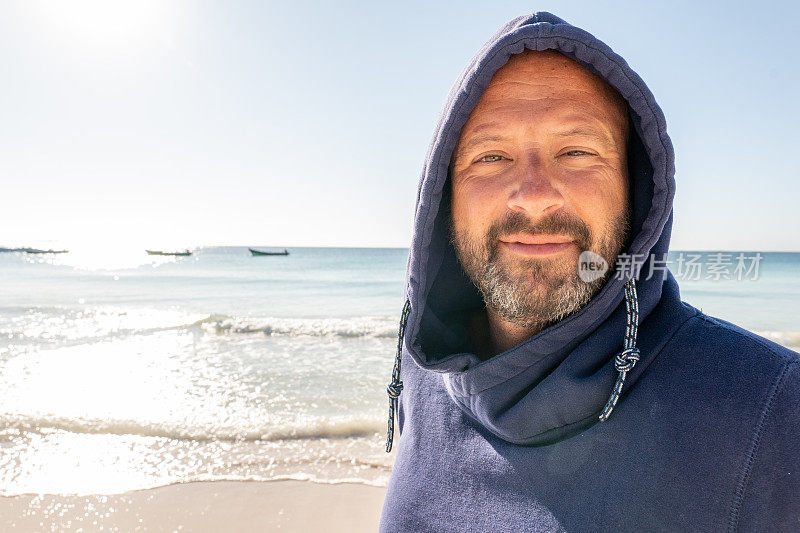 太阳升起时，一个戴着兜帽的自信男人在海滩上的肖像