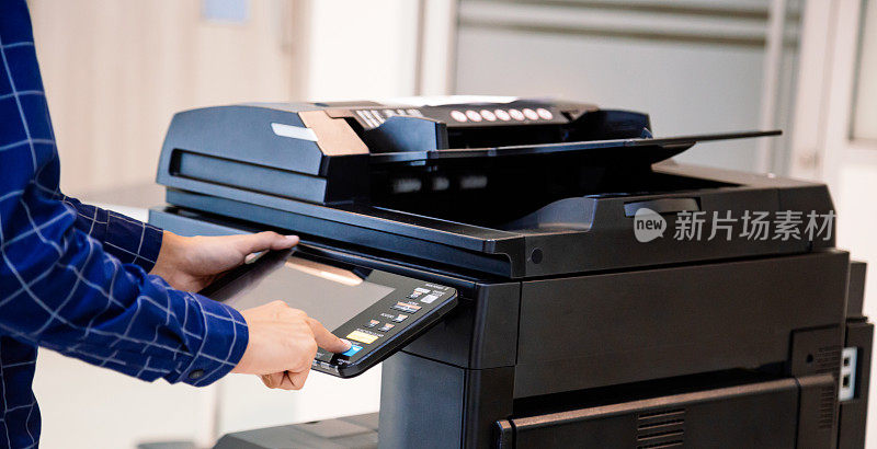 商务人士按下面板上的按钮，便可使用影印机或打印机在办公室打印或扫描文件纸张。
