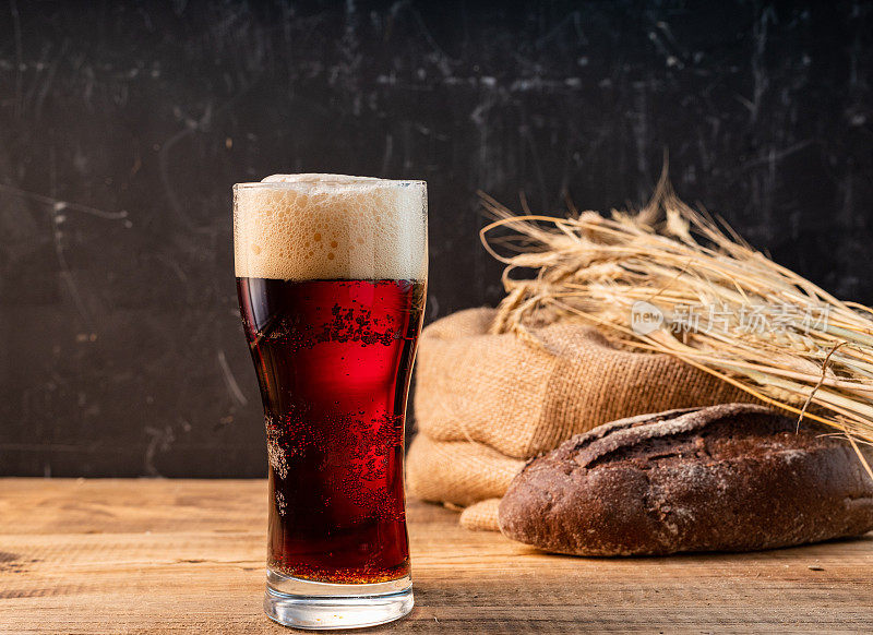 一杯黑啤酒。啤酒、小麦和黑面包。黑啤酒和面包放在木桌上。
