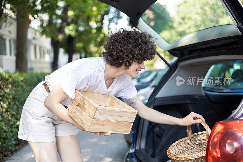 年轻女子把野餐的员工装进汽车后备箱