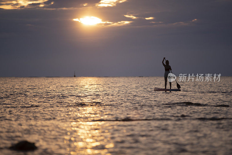 夏日里，一位女冲浪者在海中央的立板上划桨