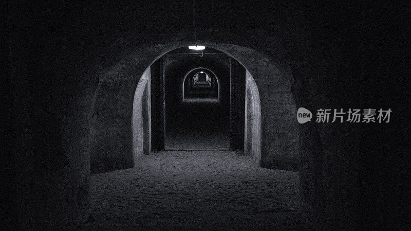 一个又长又暗的防空洞隧道，隧道的尽头有一盏灯。一个防空洞的避难所在战时黑白照片