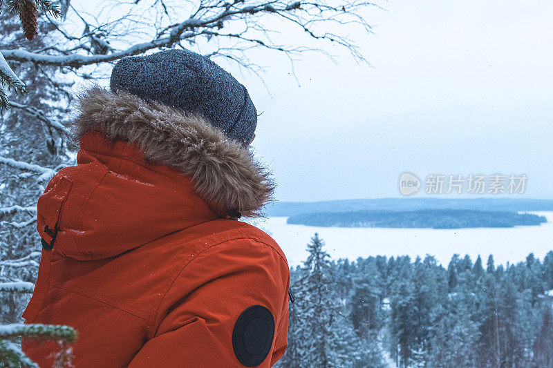 一个穿着冬装的年轻人的肖像，一件红色的夹克，背景是白雪皑皑的森林。小伙子若有所思地望着远方，欣赏着冬天的风景。