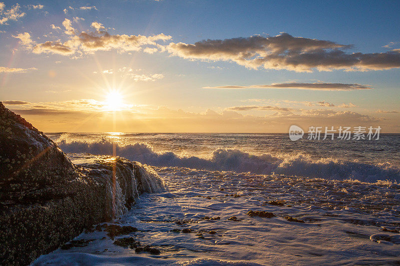 海面上明亮的日出，海浪冲刷着岩石