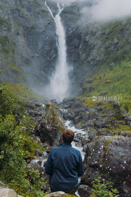 一个男人旅行者考虑在挪威瀑布风景山谷的后视图