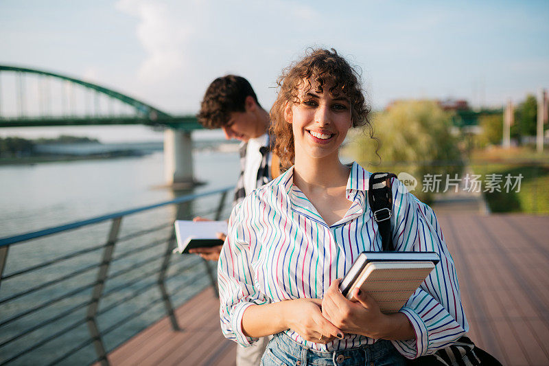 微笑的女学生拿着书站在城市的户外