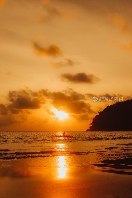 泰国普吉岛拉延海滩，夕阳西下，一个半外国人坐在海边的冲浪板上，