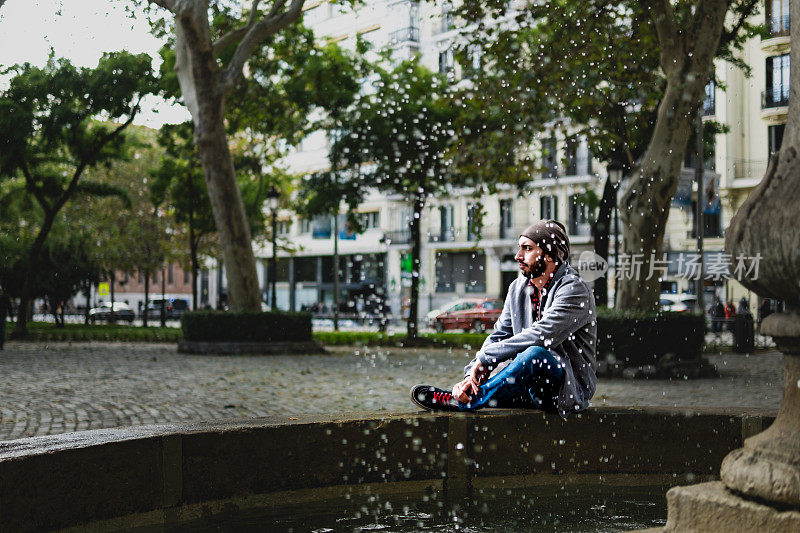 都市氛围:戴着帽子的休闲男子，坐在喷泉上，马德里街头风格。