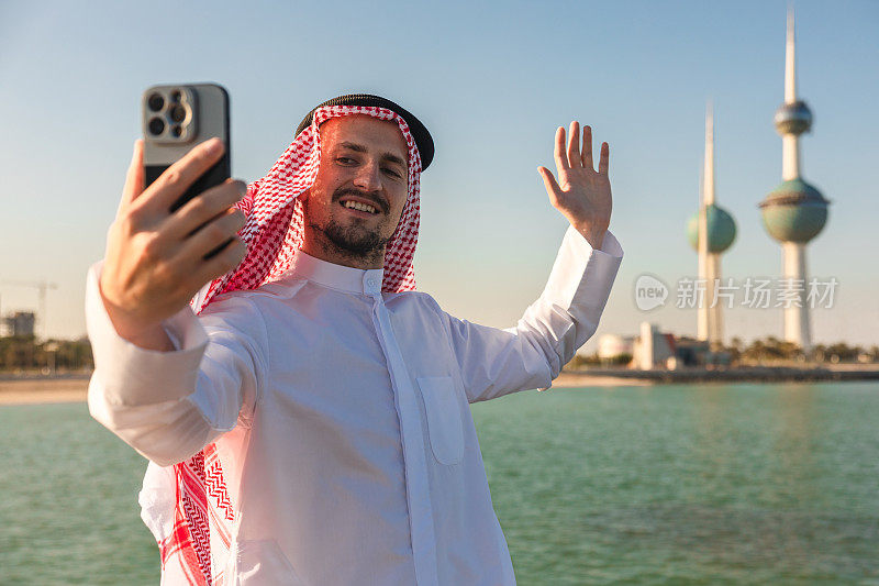 年轻的酋长在科威特海边使用他的智能手机