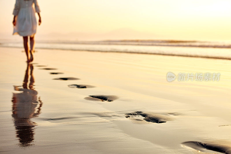 湿漉漉的沙滩上的脚印和一个在夕阳下散步的女人