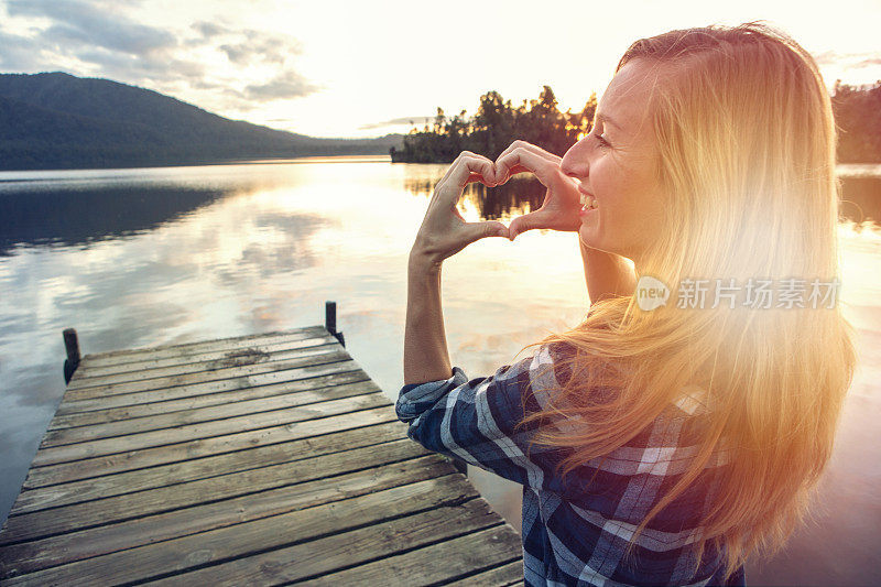 湖面上的码头上的年轻女子做了一个心形的框架