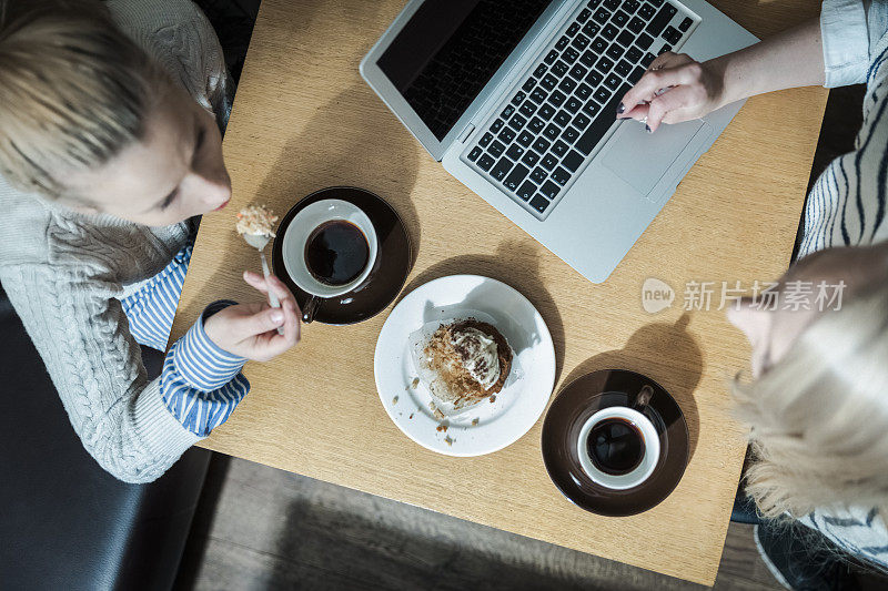 一个女人吃着松饼，而朋友在咖啡馆用笔记本电脑