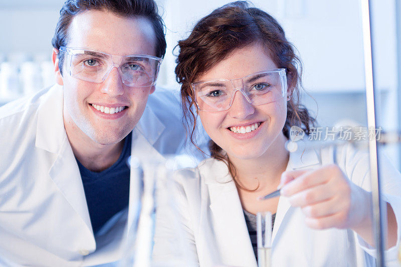 快乐的大学化学学生穿着实验室外套，做实验